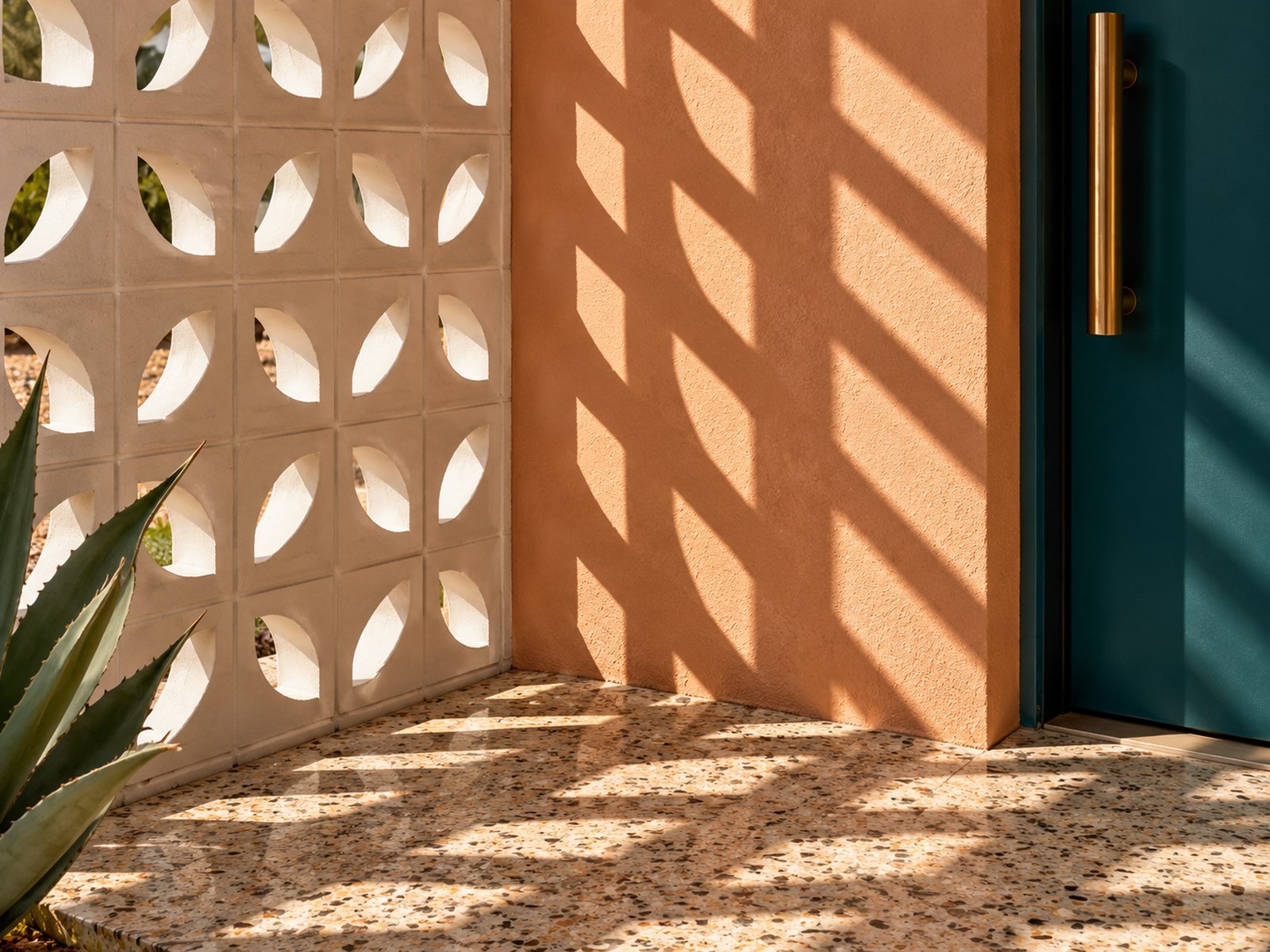 Breeze-block shadows across peach plaster and a terrazzo floor beside a teal front door with a brass handle