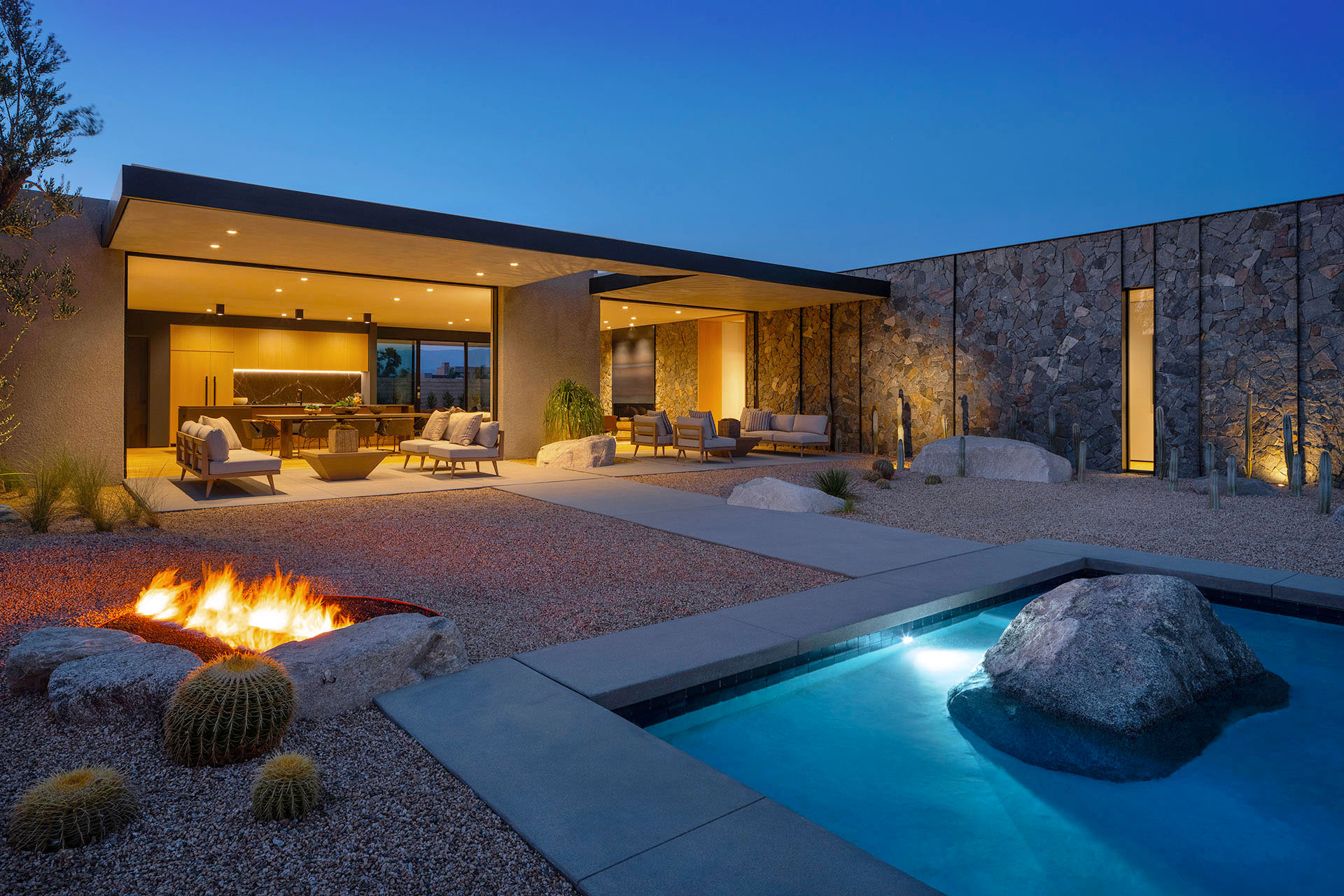 Echo Estate, a Desert Luxury Estates home in Rancho Mirage, at dusk with its fire pit, open living spaces and boulder-edged pool